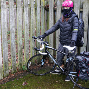 female cyclist standing in wet weather gear with bike