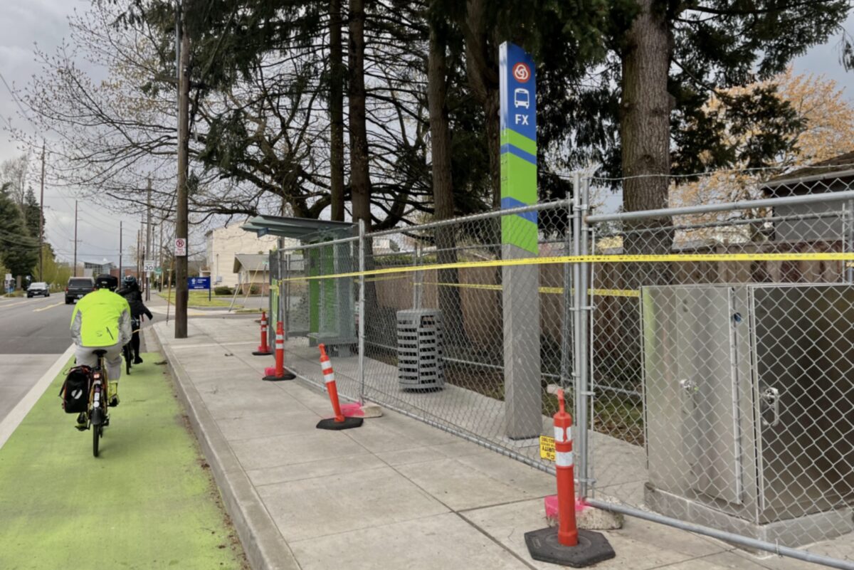 Bicycle rider in a green-painted bike lane next to a sidewalk with a bus stop under construction