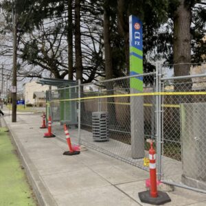 Bicycle rider in a green-painted bike lane next to a sidewalk with a bus stop under construction