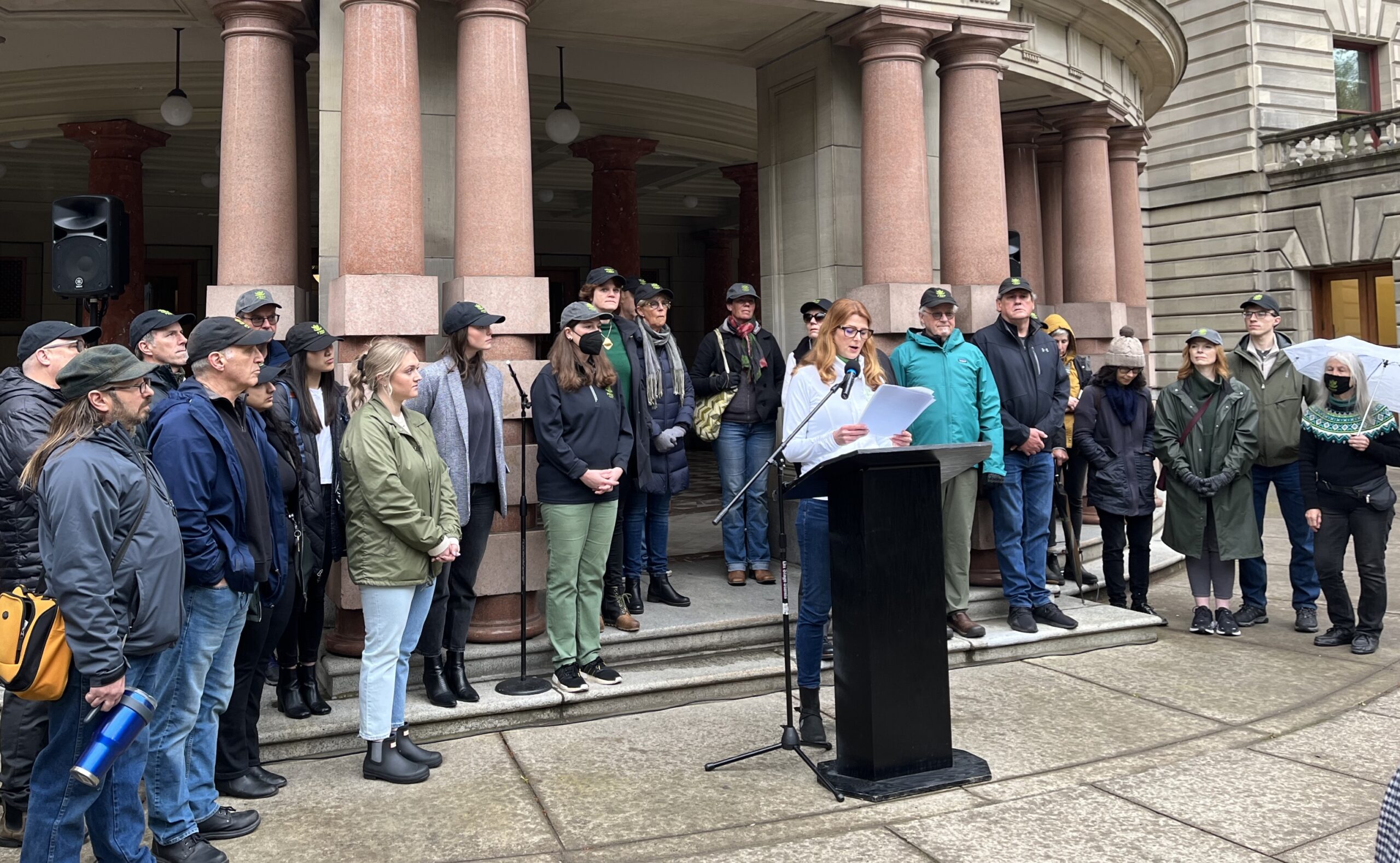 Group of people inside standing behind someone at a lectern in front of an old city building.