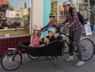 A mom and four kids in a bicycle in front of a store.