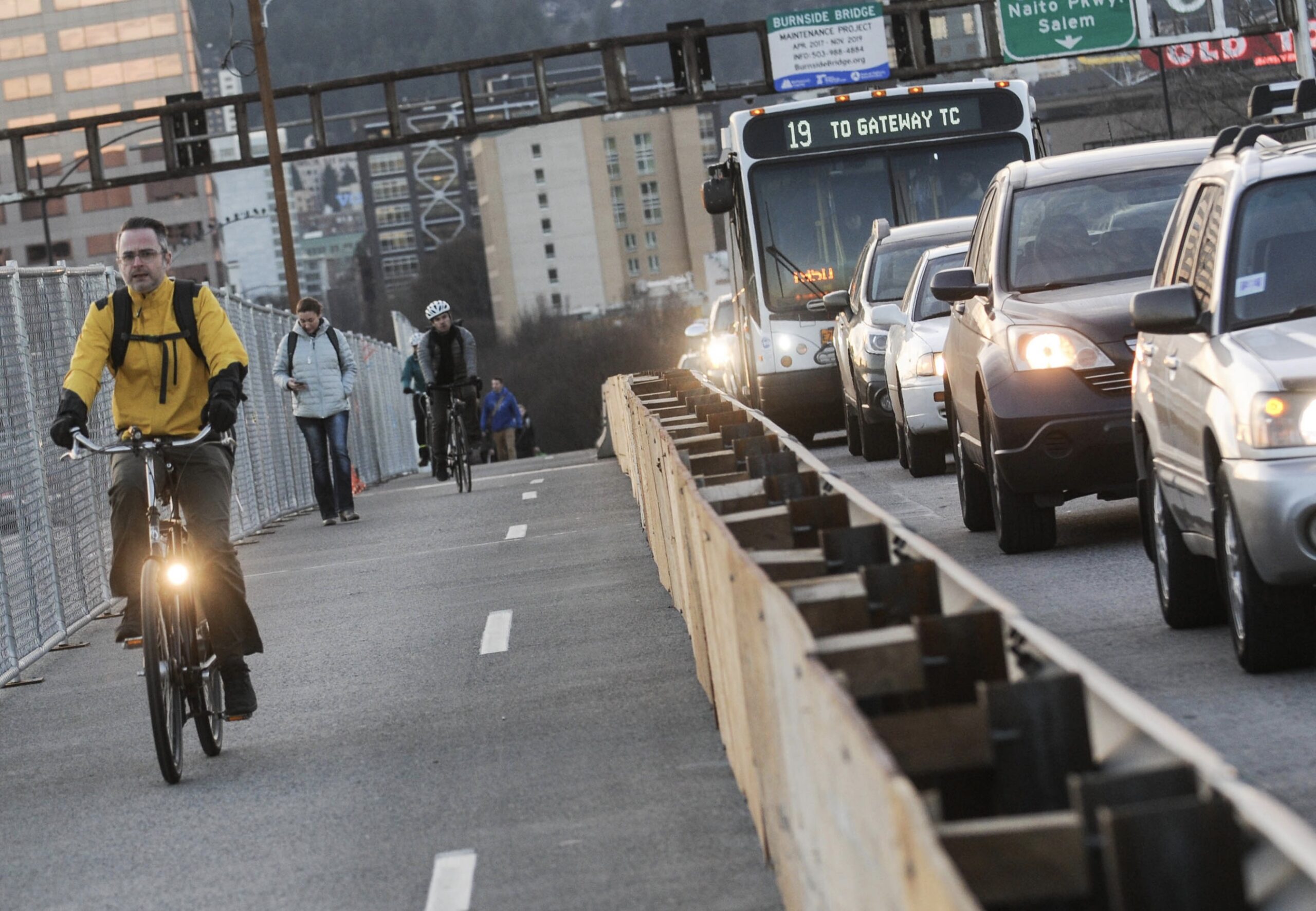 Riders in a bike path separated from other traffic lanes full of cars by a guardrail.