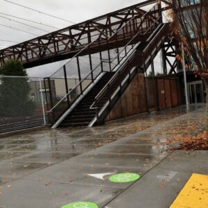 A sidewalk with a rust-colored pedestrian bridge in the background.