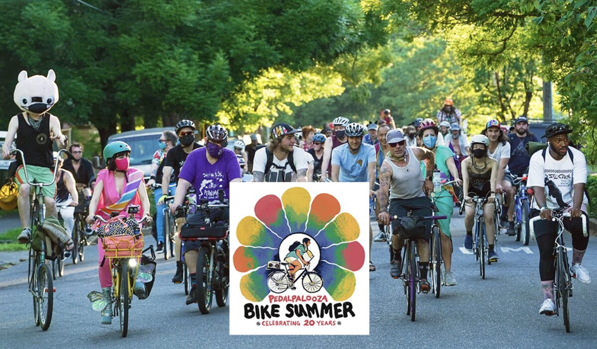 Large group of bicycle riders in a small street lined with trees.