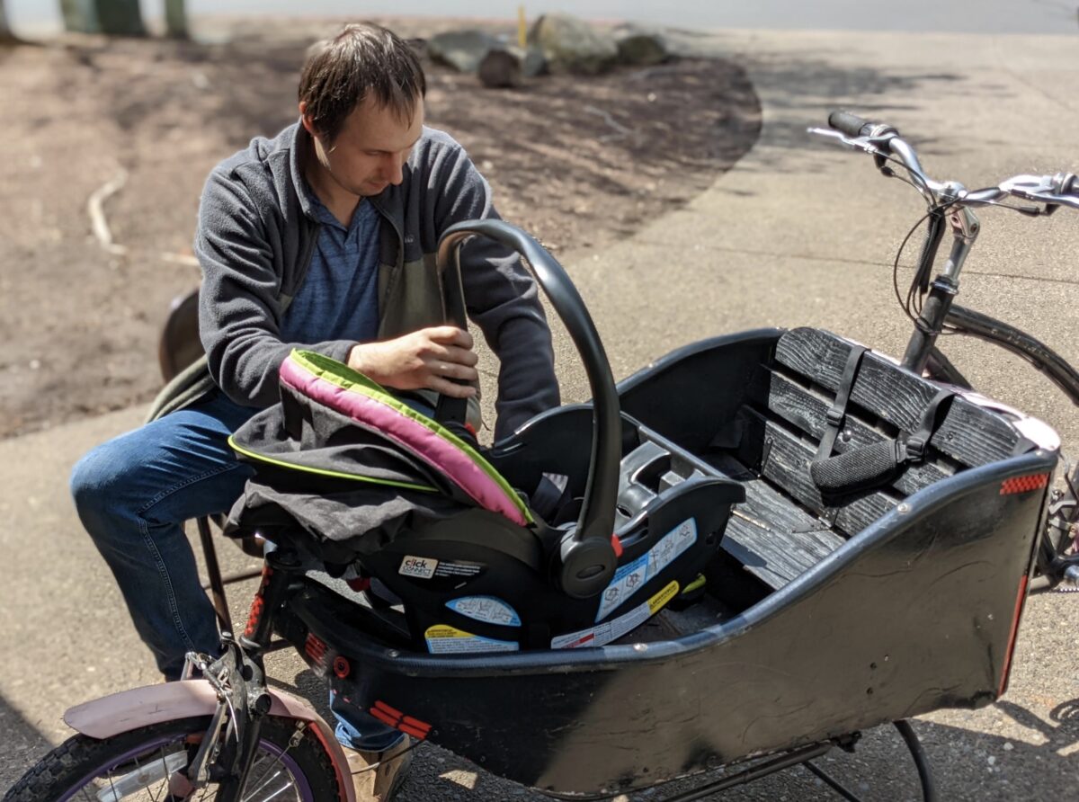 Person placing a child car set into the cargo box of a bicycle in a driveway.