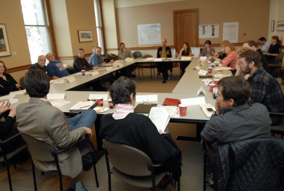 Many people sitting at desks in a circle in a conference room.