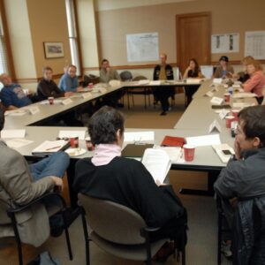 Many people sitting at desks in a circle in a conference room.