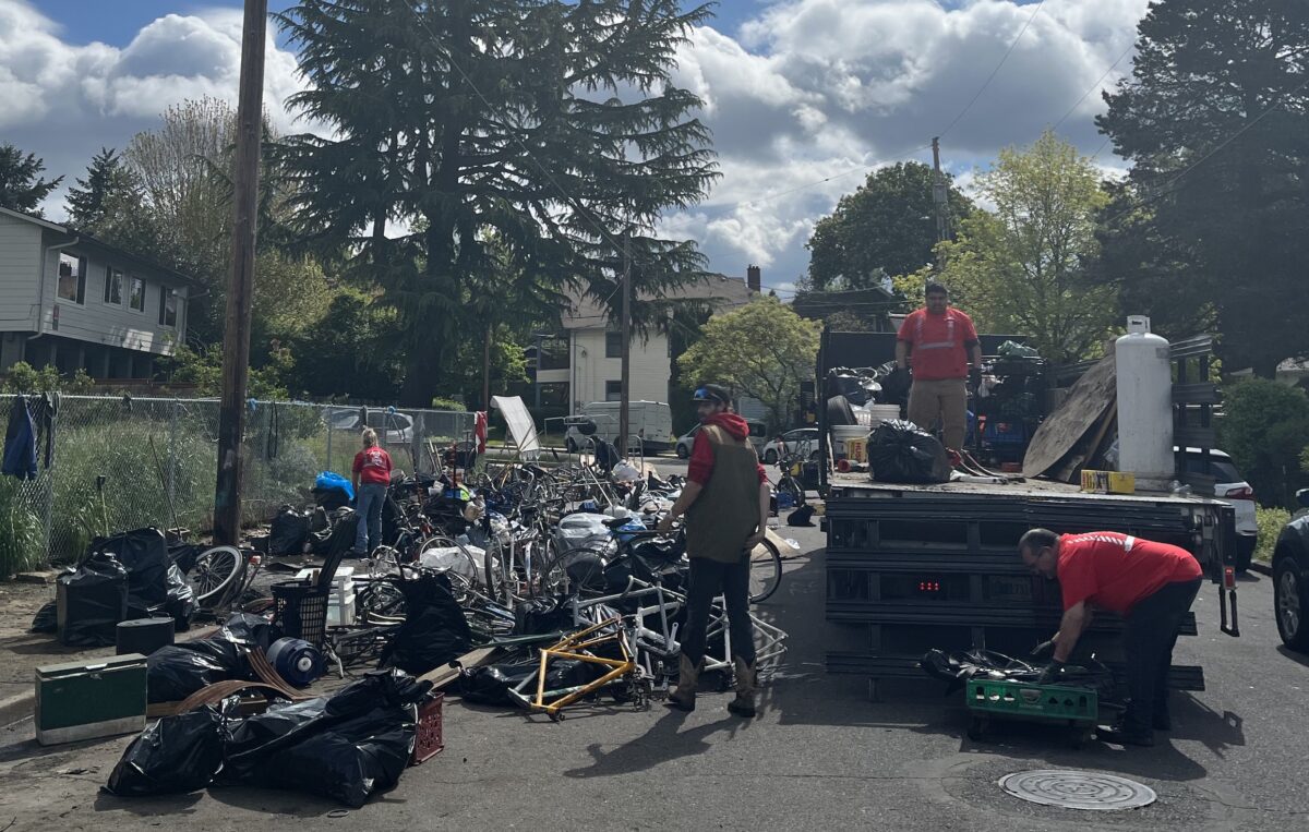 Truck with people loading bicycles and bike parts into it from a pile on the sidewalk.