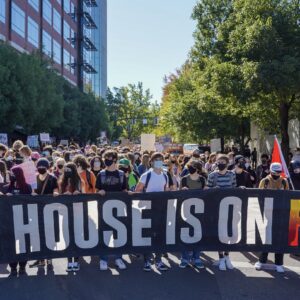 Group of protestors marching in the street with a banner that reads "Our house is on fire".