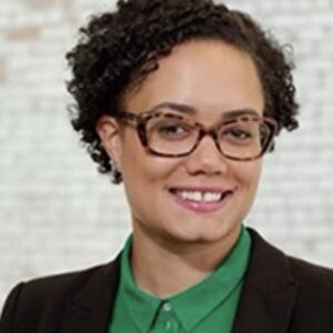 Portrait of a person with black curly hair and glasses standing in front of a white background