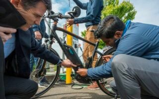 Two people crouched next to an electric bike fiddling with its battery.