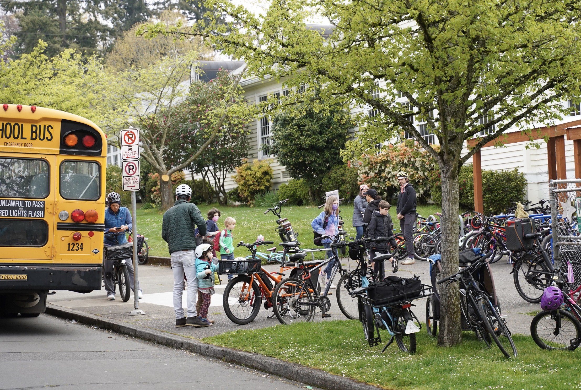 Front of elementary school with a yellow bus and bikes and people parked.