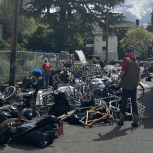 Truck with people loading bicycles and bike parts into it from a pile on the sidewalk.