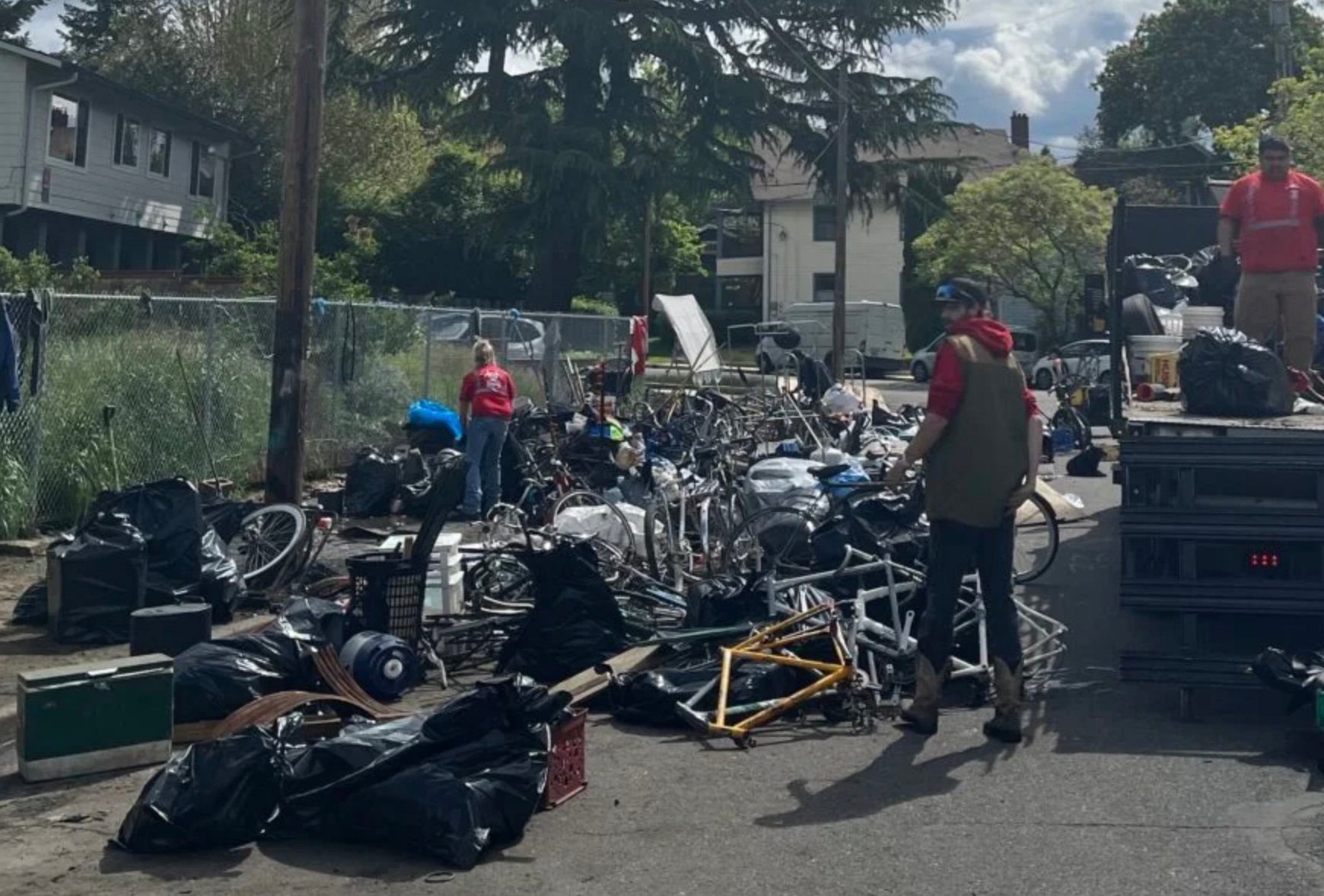 Truck with people loading bicycles and bike parts into it from a pile on the sidewalk.